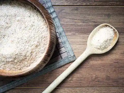 Psyllium husk in a wooden bowl and wooden spoon, against a wooden background
